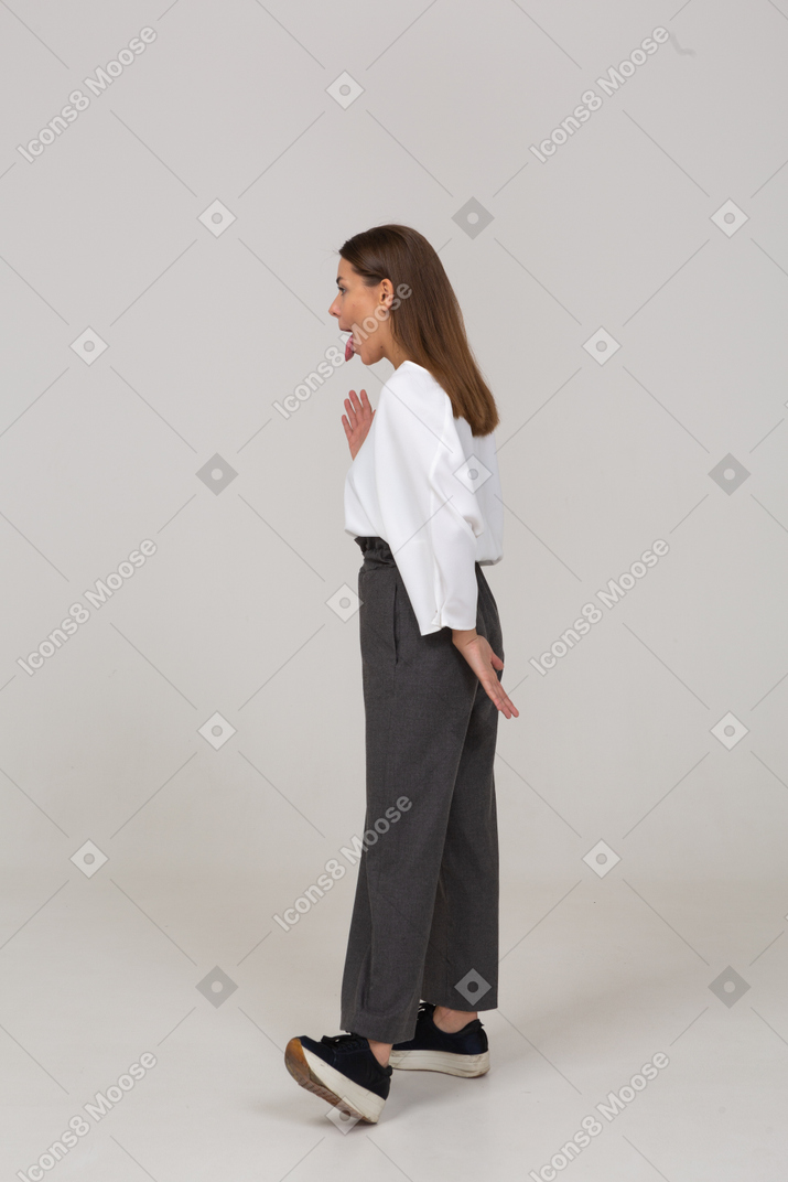 Side view of a young lady in office clothing showing tongue and raising hand