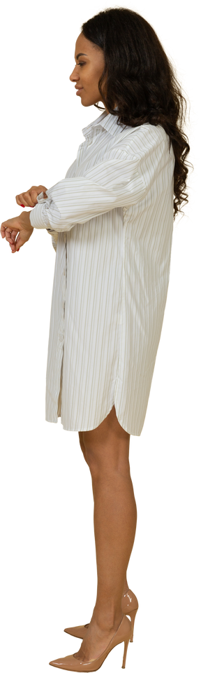 Vista lateral de uma jovem mulher de pele escura em um vestido branco abotoando a manga