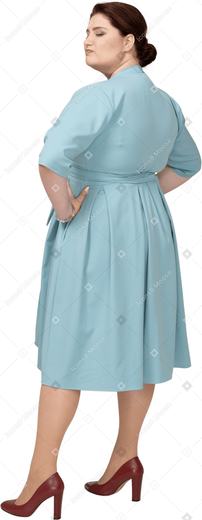 Rear view of a woman in blue dress posing with hands on hips