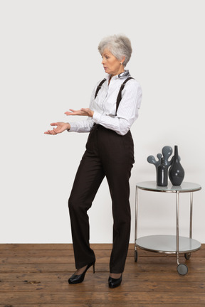 Вид спереди пожилой женщины в офисной одежде, указывающей в сторону