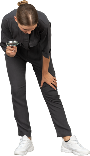Front view of a young woman in a jumpsuit holding a magnifying glass