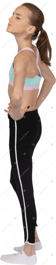 Dreiviertel-rückansicht eines jugendlichen mädchens in sportbekleidung, das hände mit geschlossenen augen auf hüften legt
