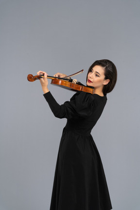 Close-up de uma jovem alegre de vestido preto tocando violino