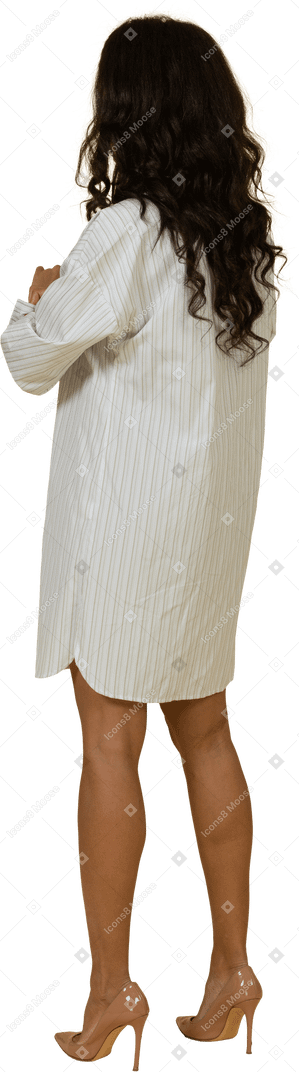 Vue de trois quarts d'une jeune femme à la peau sombre en robe blanche retroussant ses manches