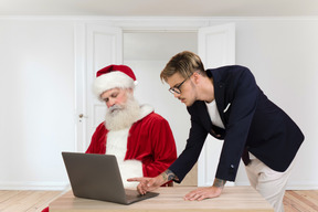 Papai noel está dormindo enquanto o homem está trabalhando com laptop