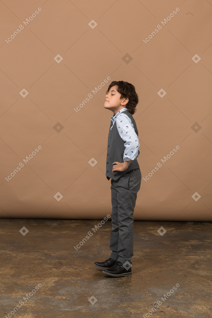 一个穿着灰色西装的男孩双手叉腰站立的侧视图