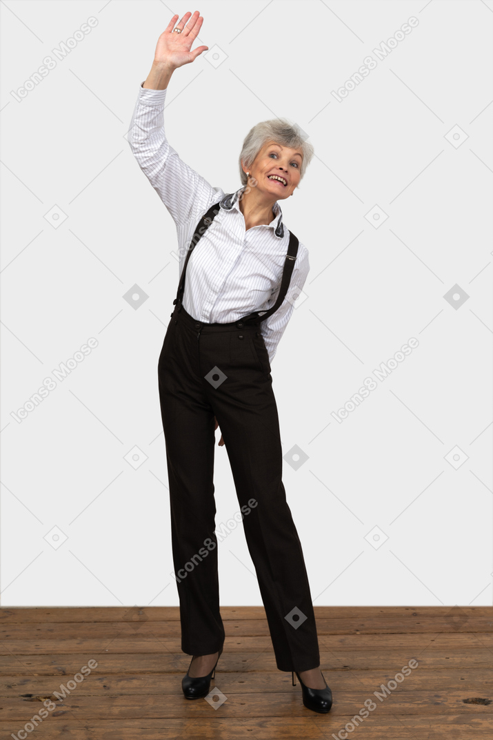 一位老太太在做问候手势举起她的手的办公室衣服的前视图