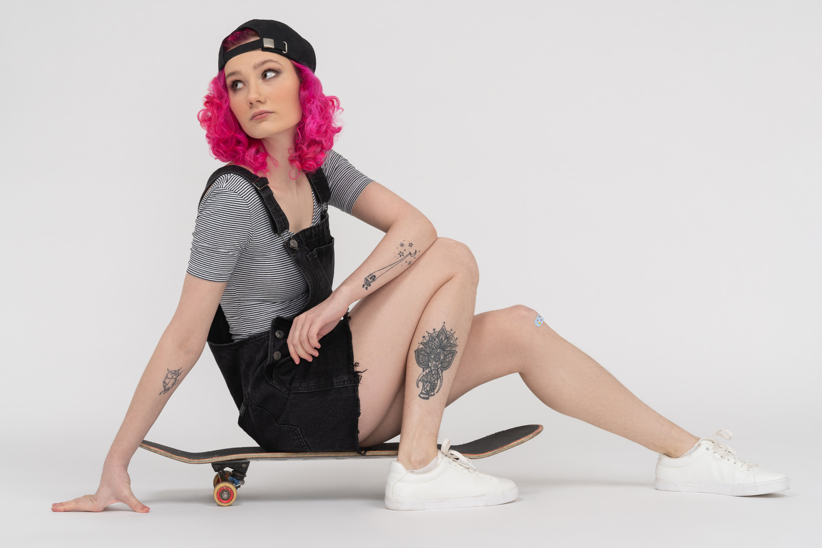 Tattooed girl with pink hair sitting on a skateboard