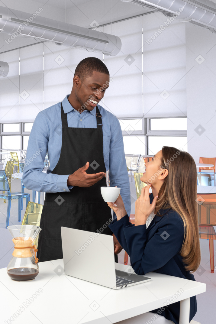 Handsome barista chatting with an attractive girl in cafe interior