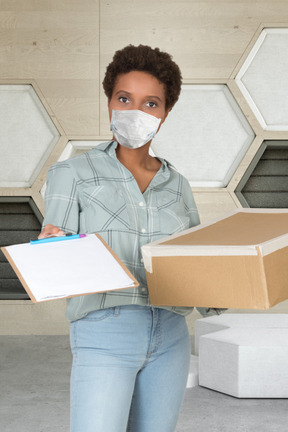 A woman wearing a face mask and holding a box