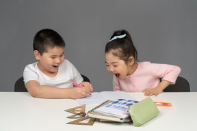 Menino e menina rindo enquanto fazem lição de casa