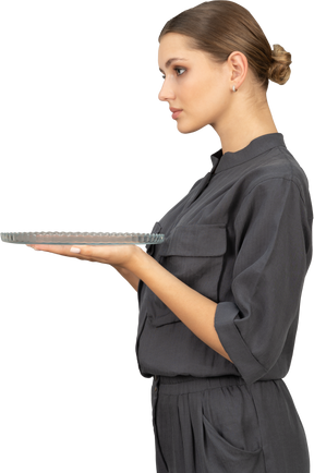 Side view of a young woman in a jumpsuit holding glass plate