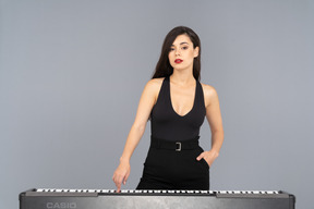 Front view of a young lady in black dress pressing the key of a piano