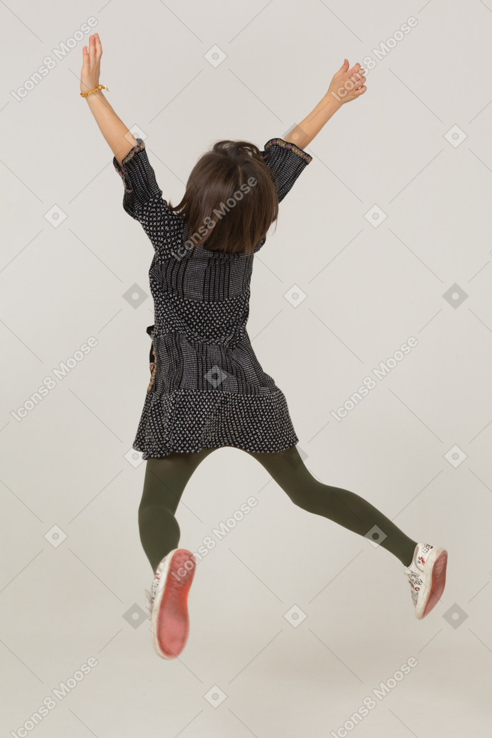 Back view of a jumping little girl in dress outspreading hands and legs