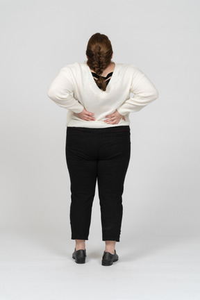 허리 통증으로 고통받는 흰색 스웨터에 통통한 여자의 후면보기