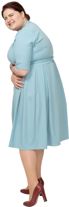 Vista lateral de uma mulher de vestido azul sofrendo de dor de estômago
