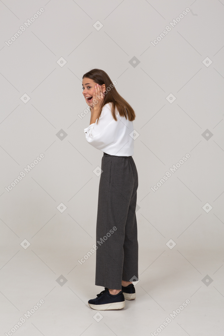 Vista laterale di una giovane donna eccitata in abiti da ufficio che tocca il viso