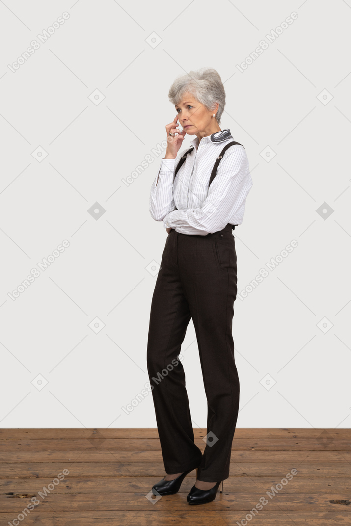 Vue de trois quarts d'une vieille dame réfléchie en vêtements de bureau touchant le visage