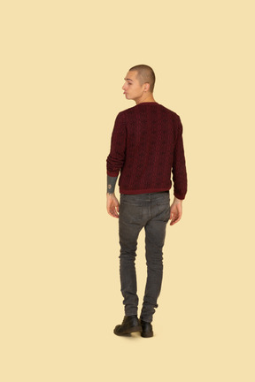 Back view of a grimacing young man in red pullover looking aside