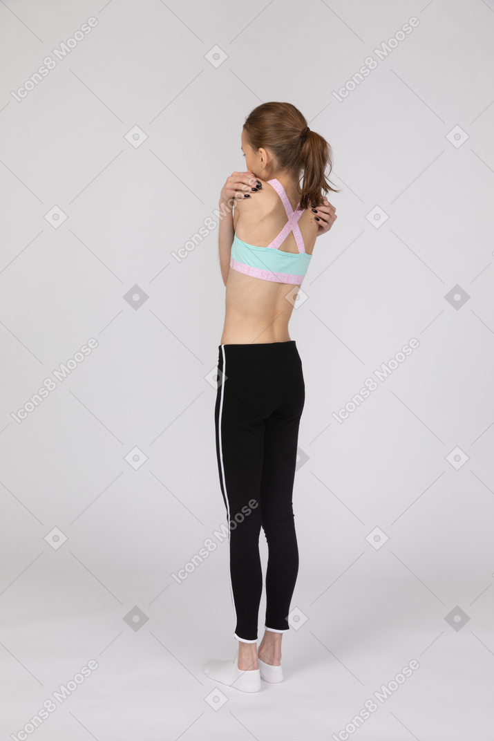 Back view of a teen girl in sportswear embracing herself