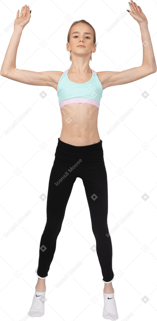 Vista frontal de uma adolescente em roupas esportivas pulando e levantando as mãos
