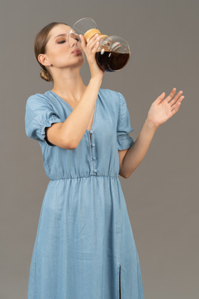Three-quarter view of a young woman in blue dress drinking wine out of a pitcher