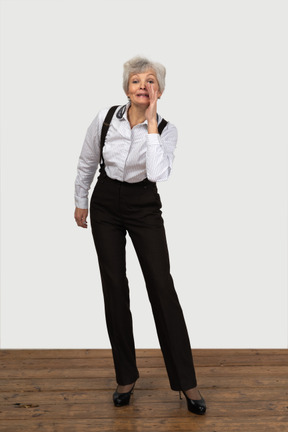 Front view of an old female in office clothes standing still in the room and telling a secret