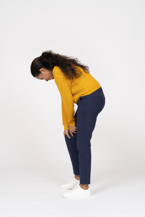 Side view of a girl in casual clothes bending down and touching her hurting knee