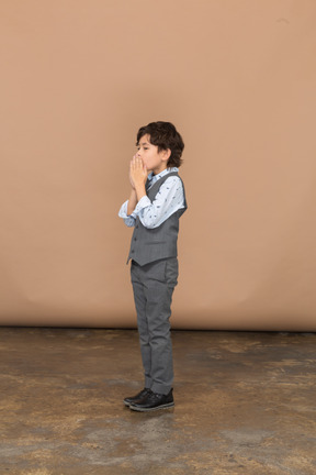Вид сбоку на мальчика в костюме, делающего молитвенный жест