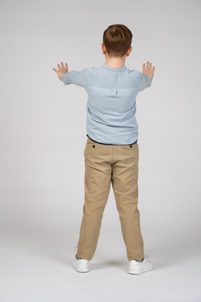 Вид сзади на мальчика, стоящего с вытянутыми руками