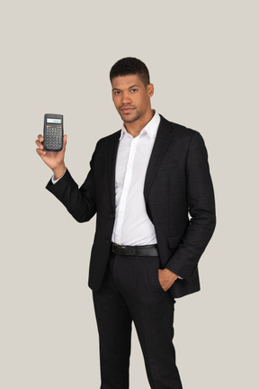 Young man in black suit pointing at calculator he's holding