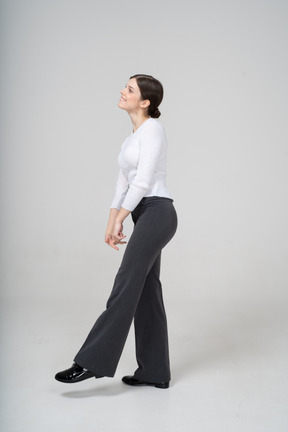 한쪽 다리에 균형 잡힌 검은색 바지와 흰색 블라우스를 입은 여성의 측면