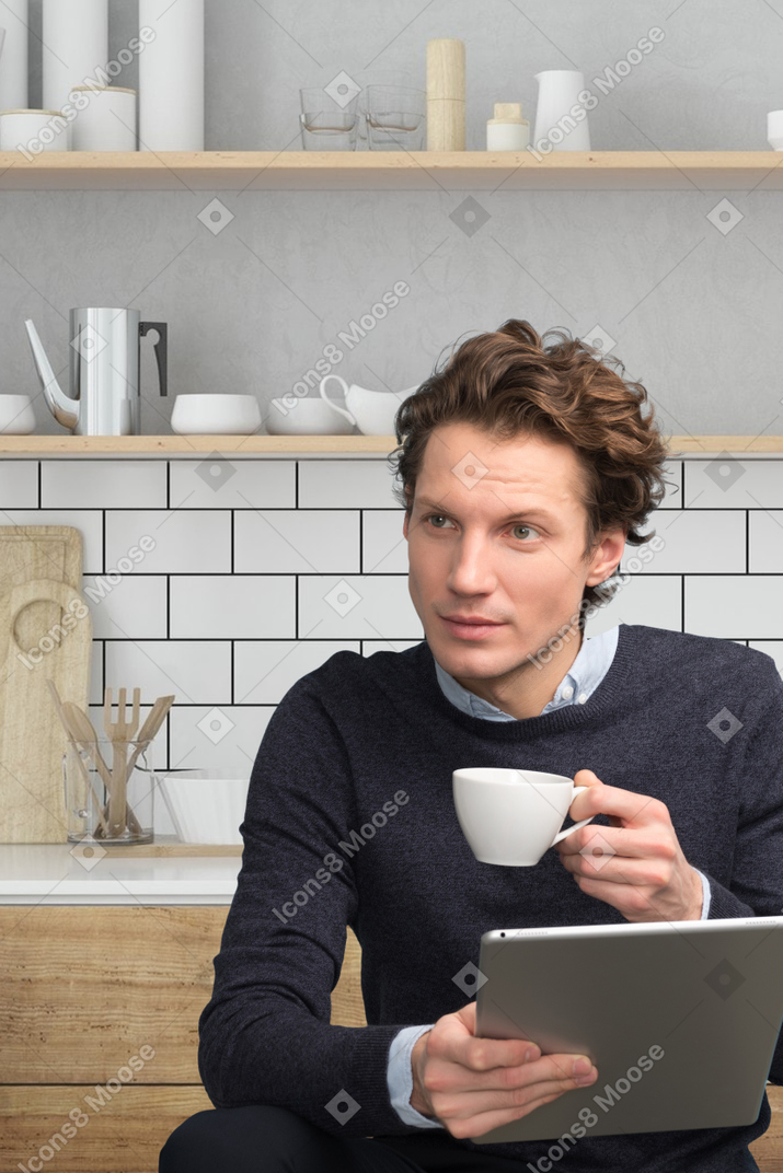 A man holding a cup of coffee while looking at a tablet