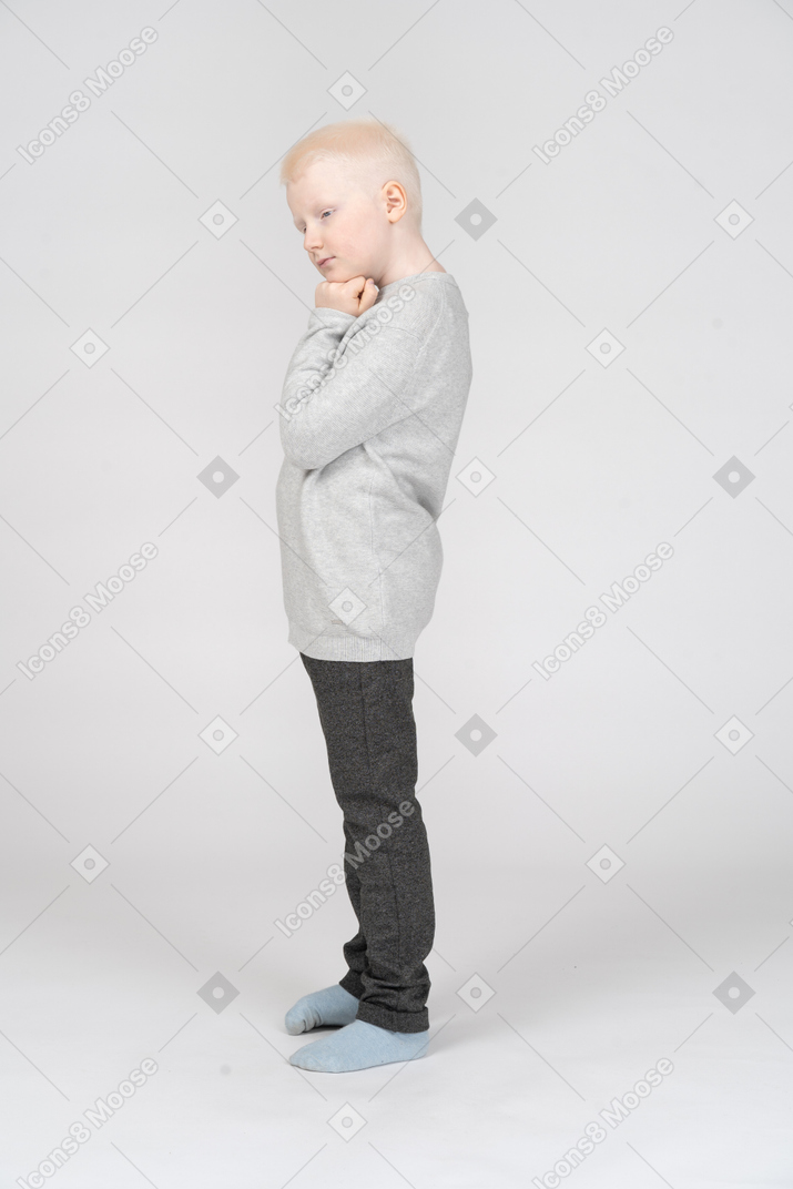 Vista lateral de un niño chico pensativo tocando la barbilla