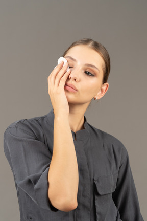 Front view of a young woman in a jumpsuit removing eye make-up