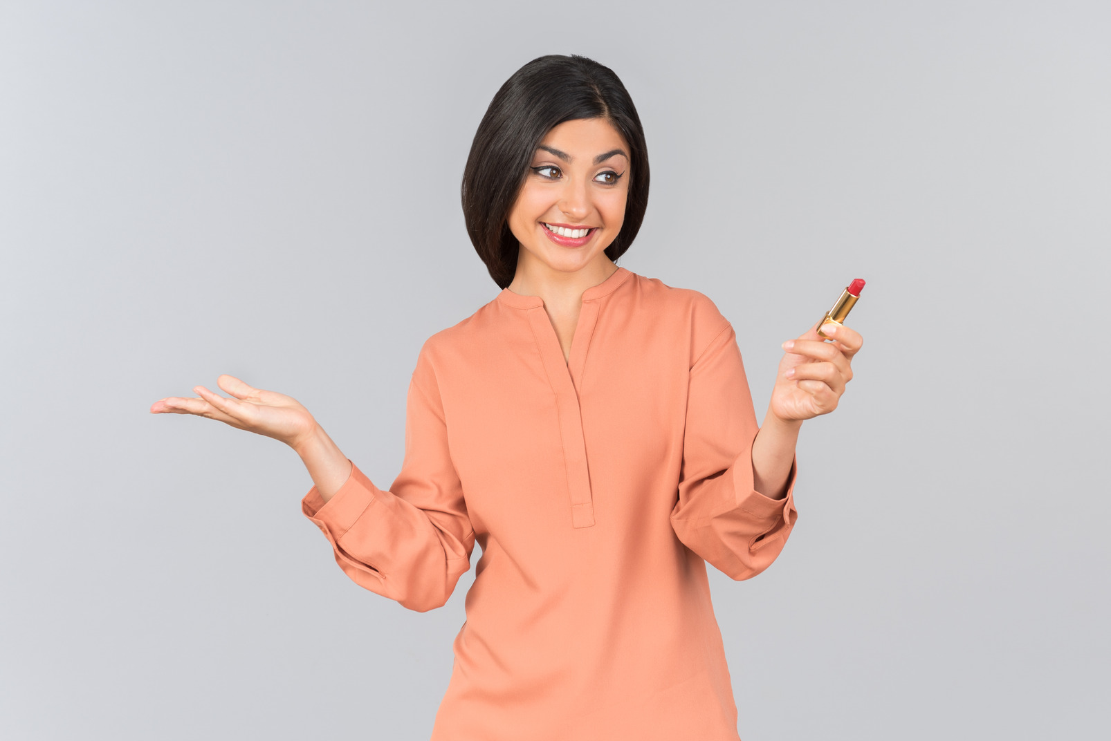 Indian woman in orange top wearing lipstick and holding one