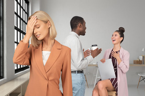 A woman is keeping her hand near her brow and woman on the chair with a laptop is laughing with a black man drinking coffee