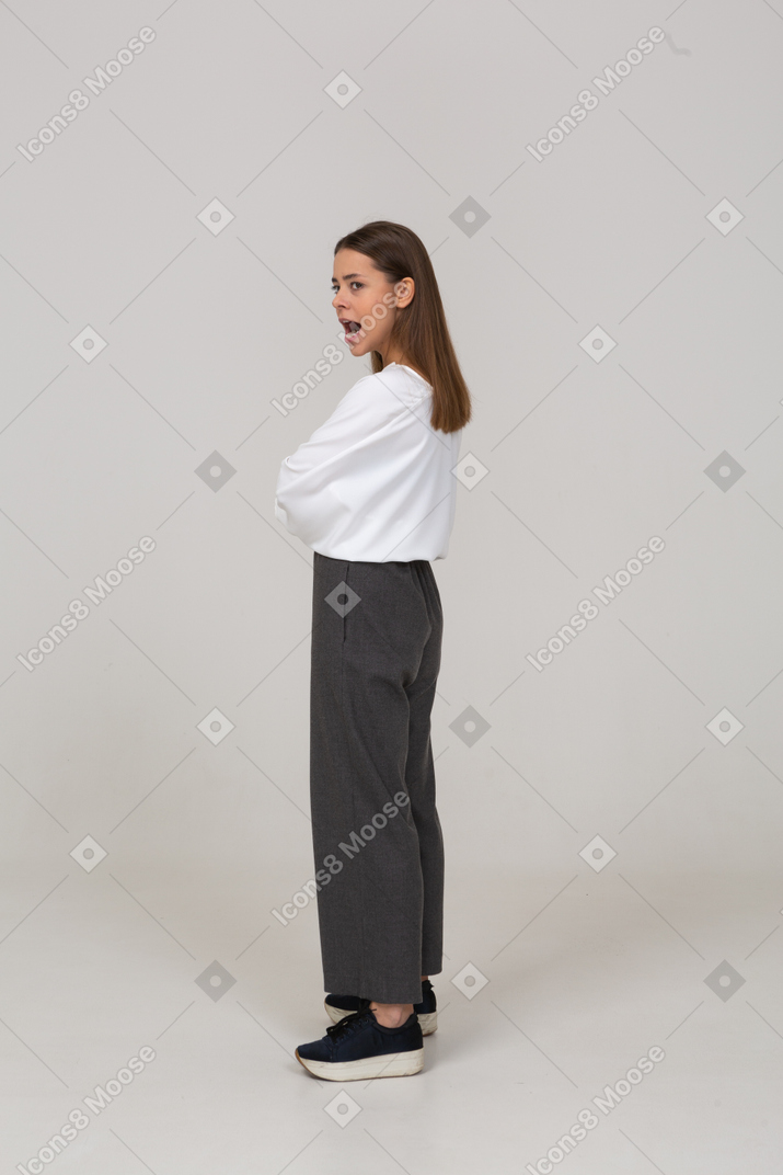 Vista laterale di una giovane donna in abiti da ufficio in piedi con la bocca spalancata