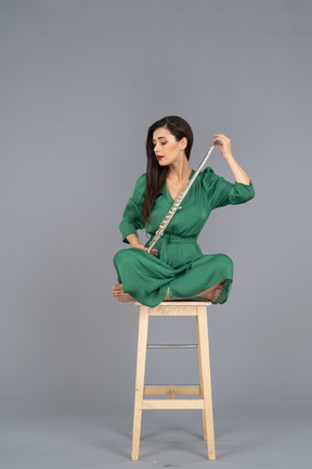 Full-length of a young lady looking at the clarinet sitting with her legs crossed on a wooden chair