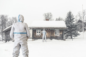 Men in protective suits standing under snowfall near wooden house