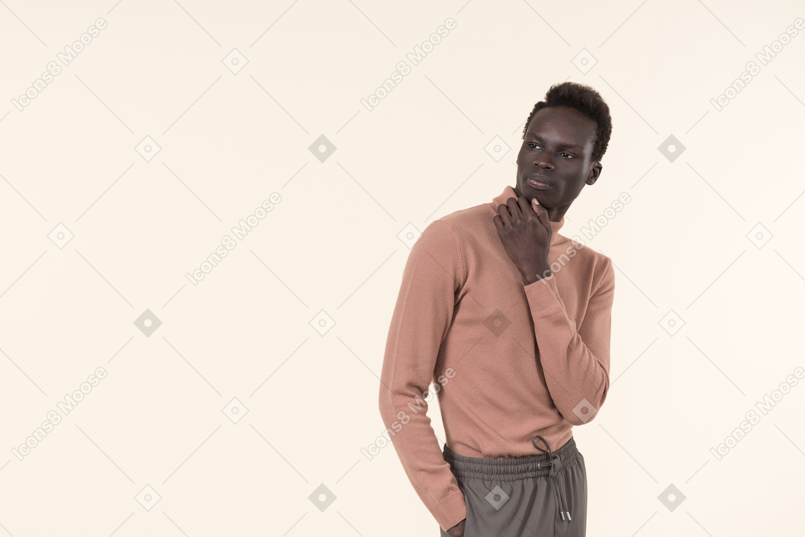 A young black man in a beige turtleneck and grey sweatpants standing casually on the white background
