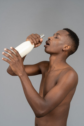 A shirtless young man drinking milk