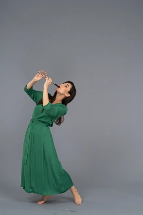 Three-quarter view of a young lady in green dress playing flute while leaning back
