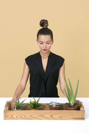 Mujer hermosa joven sentada junto a una caja de madera con algunas plantas caseras en ella