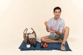 兴奋的年轻白人男子在野餐时吃水果
