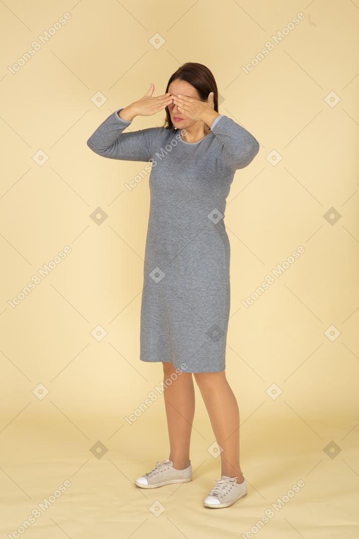 Side view of a woman in grey dress closing her eyes with hands