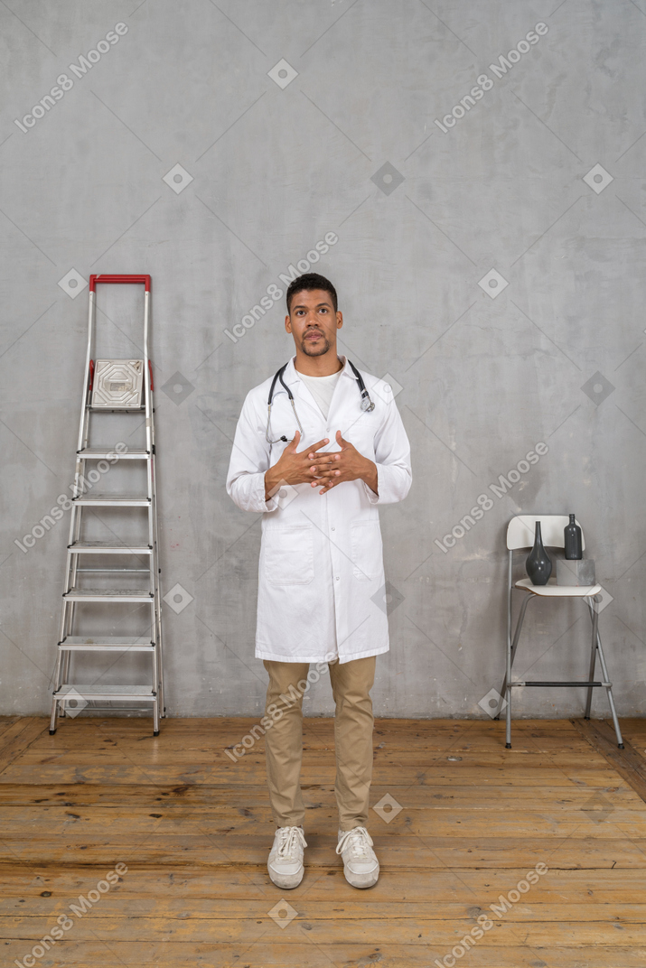 Vista frontale di un giovane dottore in piedi in una stanza con scala e sedia
