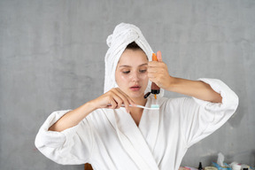 Woman in bathrobe squeezing toothpaste out of tube