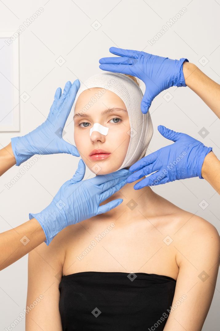 Young woman with head bandage surrounded by hands