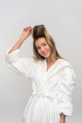 Bella giovane donna raccogliendo i capelli con spazzola per capelli rotonda